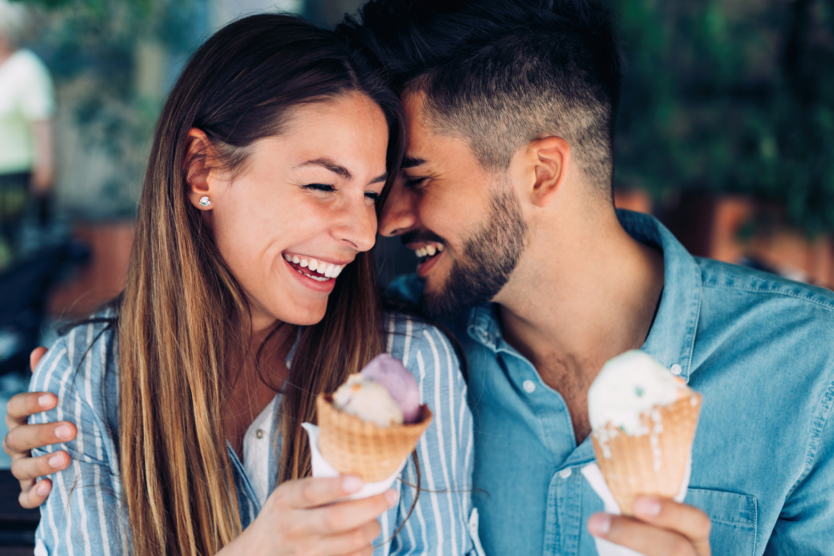 A happy couple smiles while eating ice cream cones. 