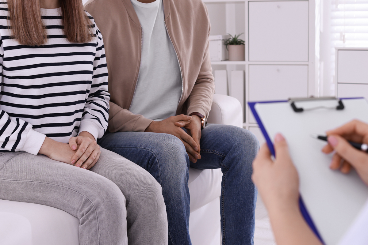 A couple sitting on a couch discusses fertility options with a fertility doctor. 